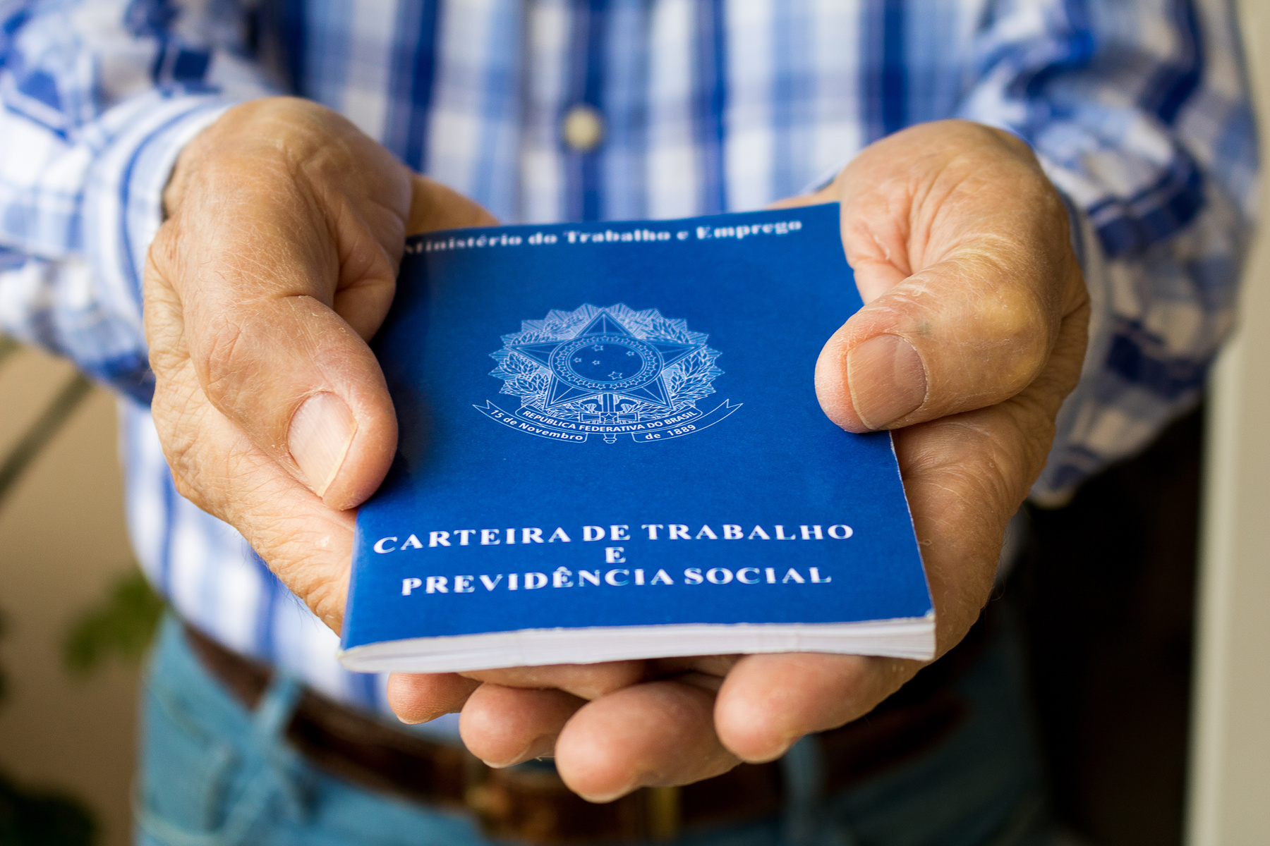Elderly old male hands worker holding portfolio work permit of Ministry of Labor and Social Security of Brazil(Translation: 'Work Permit, Ministry of Labor and Social Security of Brazil CTPS').